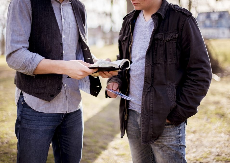 A closeup shot of two males standing near each other and reading the bible with a blurred background