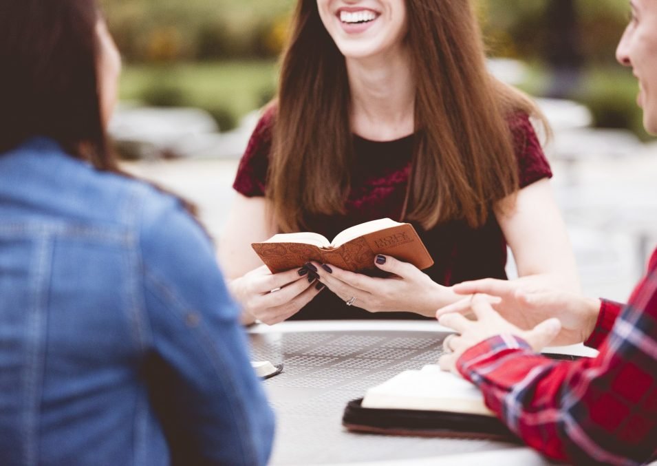 A closeup shot of females sitting around a table and reading the holy bible with a blurred background